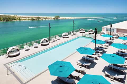 Luxury oceanfront resort pool with turquoise umbrellas, cabanas, and crystal-clear water with beach beyond