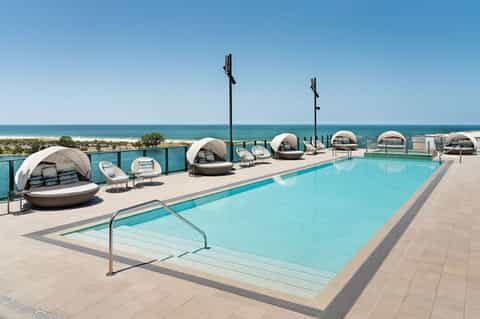 Oceanfront pool with cabanas, lounge seating, and beach horizon at daytime