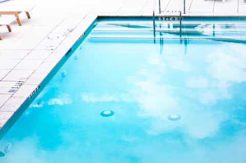 Olympic-sized swimming pool with lane markings, clear turquoise water, and white deck area with lounge chairs