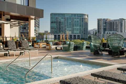 Urban rooftop spa area with hot tub, lounge seating, fire pit, and downtown cityscape views