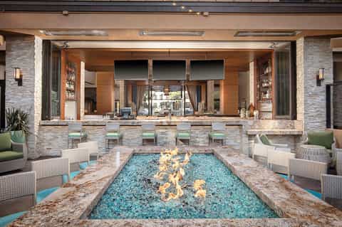 Modern outdoor bar with stone fireplace, turquoise fire feature, and lounge seating area