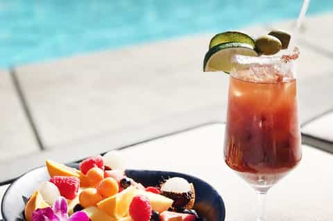 Tropical cocktail with lime garnish and salted rim by poolside with fruit plate