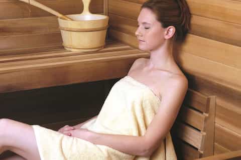 Woman relaxing in wooden sauna with towel, enjoying spa amenities in wooden interior