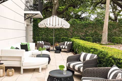 Elegant patio with white furniture, striped umbrella, wicker chairs, and manicured garden
