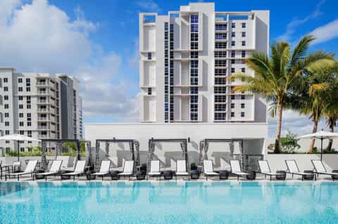 Modern resort pool with turquoise water, white high-rise hotel building, palm trees, and lounge chairs in foreground