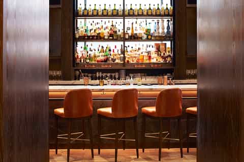 Upscale bar interior with illuminated shelving, wood paneling, and orange bar stools.