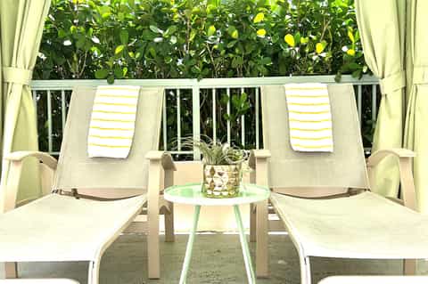 Private balcony with two lounge chairs, yellow striped towels, and tropical vegetation beyond railing