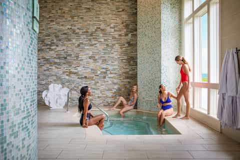 Indoor spa pool with mosaic tile walls, five people enjoying warm water bath with ocean views