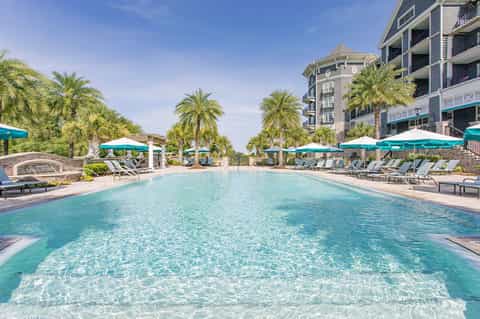 Resort pool with turquoise water, white loungers, teal umbrellas, palm trees and multi-story building