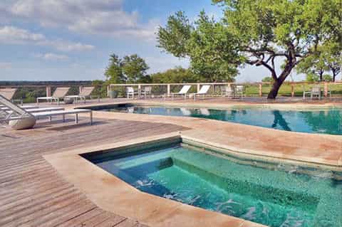 Resort pool with wooden deck, lounge chairs, and scenic countryside view with trees
