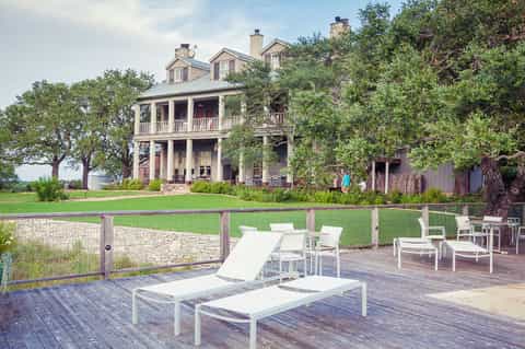 Historic farmhouse with white loungers on wooden deck overlooking manicured lawn