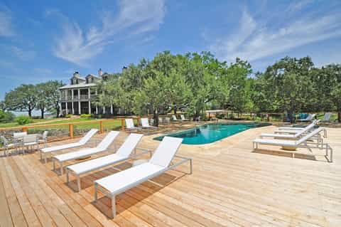 Resort pool deck with lounge chairs, vintage plantation house, and mature shade trees