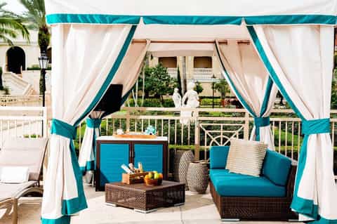 Elegant cabana with turquoise and white curtains, rattan furniture, and ocean view backdrop