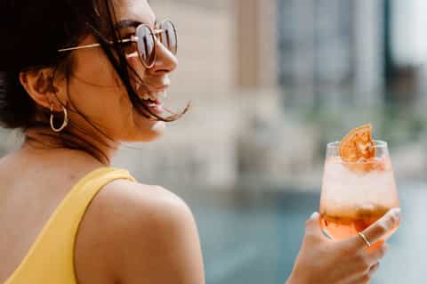 Woman in yellow swimsuit holding tropical cocktail on balcony