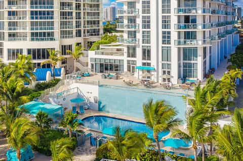 Aerial view of beachfront resort with multiple pools, tropical landscaping, and high-rise buildings