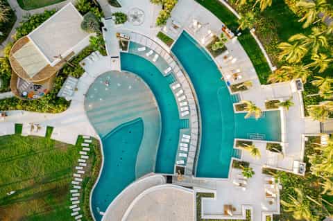 Aerial view of luxury resort with curved swimming pools, white loungers, manicured lawns, and palm trees