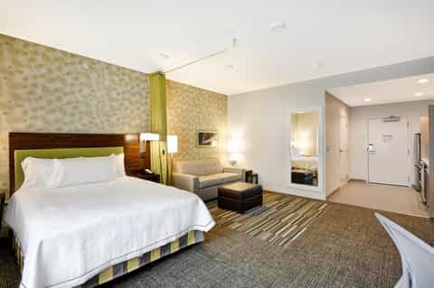 Spacious hotel suite with king bed, sitting area, patterned wallpaper, and modern furnishings