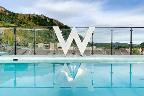 W hotel pool with large white logo, glass railings, and mountain landscape backdrop