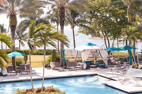 Waterfront resort pool with lounge chairs, cabanas, palm trees, and direct beach access