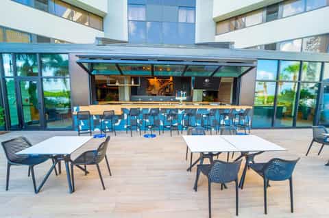 Modern resort patio with bar counter, dining tables, and glass doors overlooking waterfront
