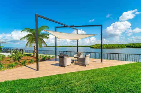 Modern pergola with shade sail overlooking calm waterway with palm trees and green lawn