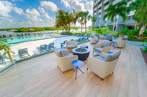 Modern resort pool deck with fire pit seating area, loungers, and views of mangroves and water