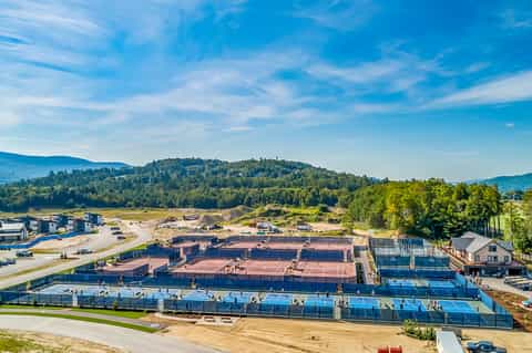 Overhead view of outdoor tennis and pickleball courts surrounded by forested hills and mountains