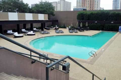 Urban hotel rooftop pool with turquoise water, lounge chairs, and city skyline backdrop