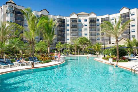 Resort pool surrounded by loungers, palm trees, and multi-story buildings
