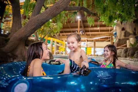 Children enjoying blue water ride attraction under large tree at indoor water park