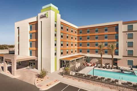 Modern hotel exterior with orange and cream colored building, pool area, and palm tree landscaping