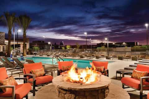 Resort pool at dusk with fire pit, orange lounge chairs, palm trees and dramatic purple sunset sky