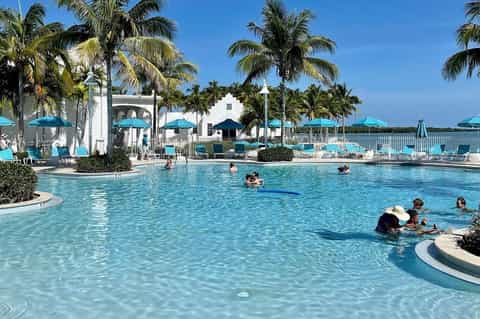 Lagoon-style resort pool with white structures, palm trees, and families swimming