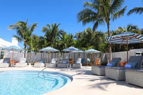 Resort pool area with blue striped umbrellas, lounge chairs, and palm trees