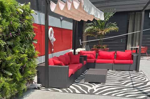 Modern patio lounge with red cushioned seating, black pergola, green living wall, and striped area rug