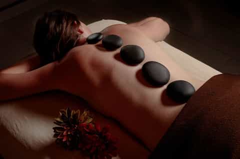 Woman receiving hot stone massage treatment on back with red flower decoration
