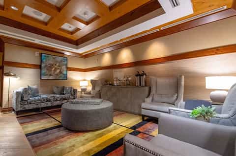 Elegant lounge with coffered wood ceiling, plush gray seating, round ottoman, and colorful geometric area rug