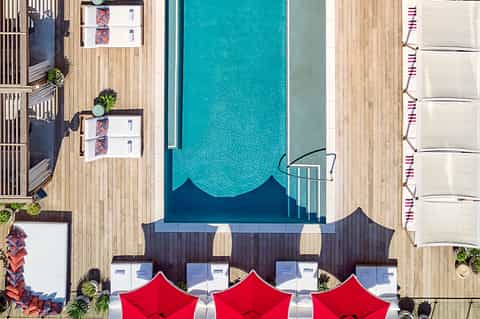 Overhead view of resort pool with red umbrellas, wooden decking, and lounging areas