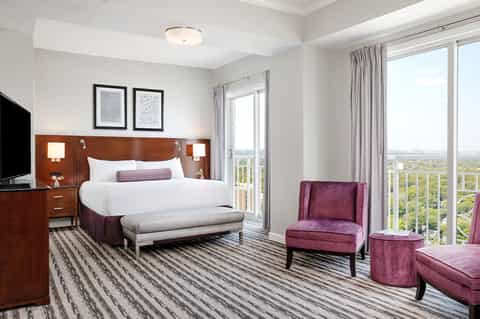 Upscale hotel bedroom with wood headboard, panoramic windows, purple accent chairs, and countryside views