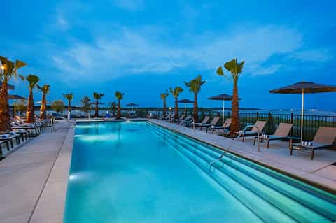 Nighttime resort lap pool with lounge chairs, palm trees, and ocean view lighting