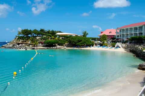 Pristine turquoise beach cove with white sand, resort buildings, and swimming area
