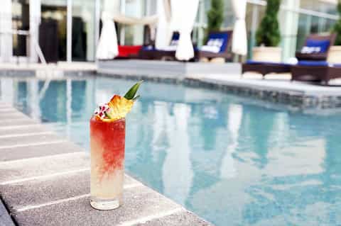 Tropical cocktail by resort pool with lounge chairs and white umbrellas in background