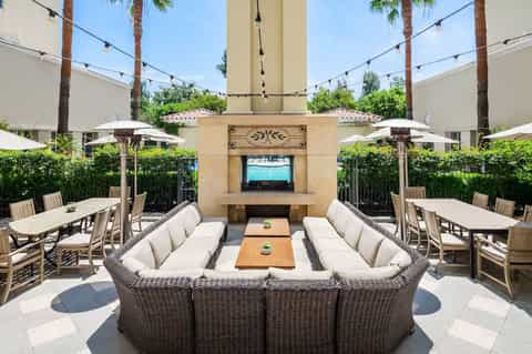 Resort courtyard with fireplace, lounge seating, umbrellas, palm trees, and television screen