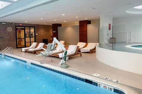 Indoor pool deck with loungers, spa entrance, and modern architectural design with skylights
