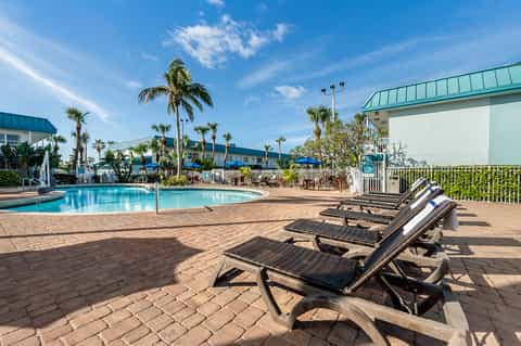 Tropical pool area with palm trees, lounge chairs, and resort buildings under blue sky