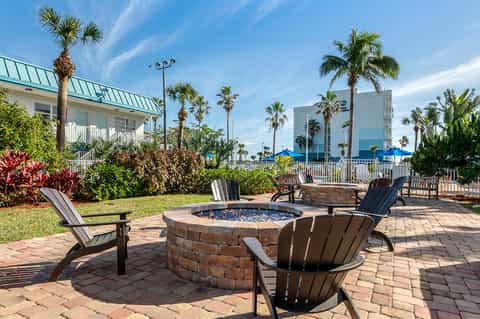 Backyard fire pit with Adirondack chairs, palm trees, and beachfront hotel in background