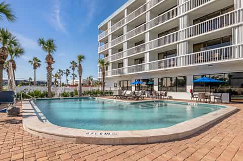 Resort pool with turquoise water, white railings, palm trees, and modern white building