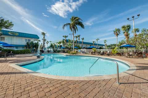 Resort pool with blue water, palm trees, white buildings, and clear blue sky