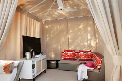 Luxury cabana room with white canopy bed, amenities, and entertainment setup