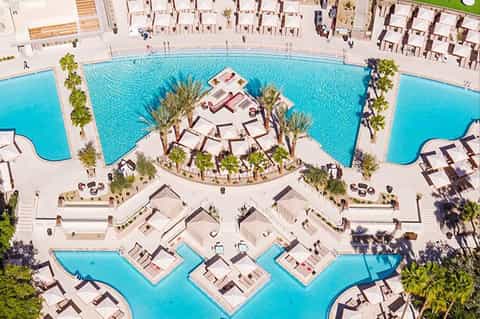 Aerial view of resort with turquoise pools, white sun loungers, palm trees, and geometric layout